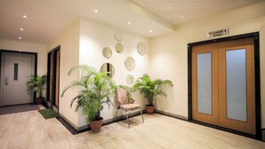 A hallway with a reception desk, a chair, potted plants, a wall with mirrors, and a sign for 'Glamour Hall'. - Hotel Konark (Indore)