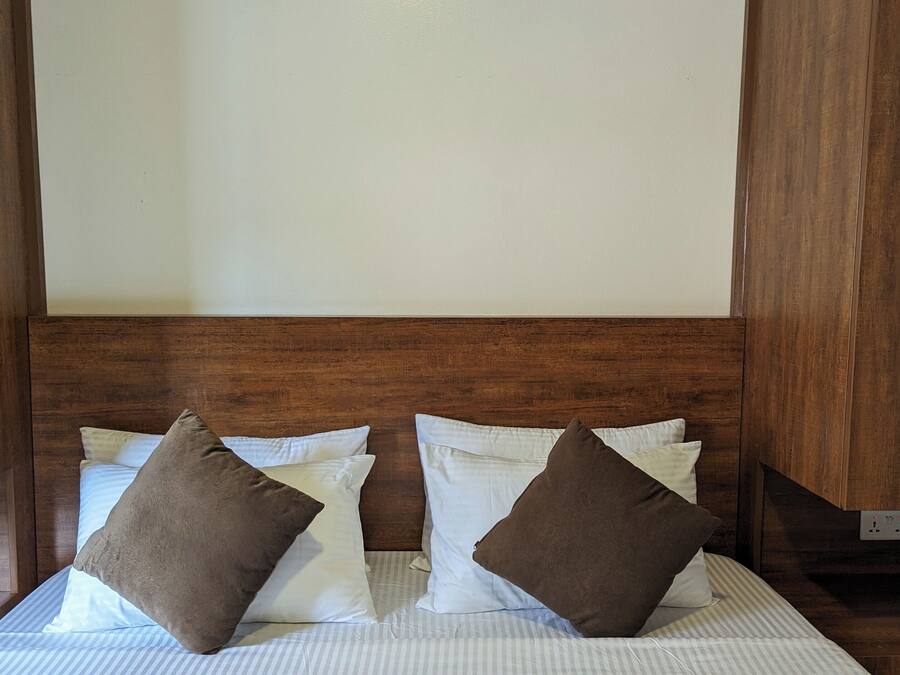 Una cama bien hecha con ropa de cama a rayas y dos almohadas marrones, frente a un cabecero y paredes de madera.