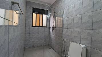 Un baño con baldosas de mármol gris, una ventana con barrotes negros, una ducha y un inodoro.