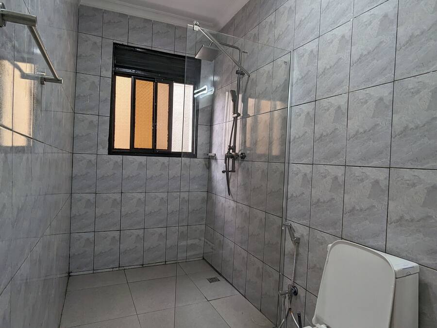 Un baño con baldosas de mármol gris, una ventana con barrotes negros, una ducha y un inodoro.