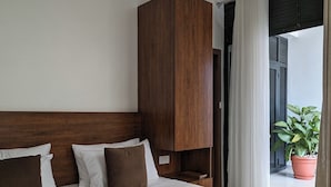 Habitación de hotel con una cama grande, cabecero de madera y una planta en maceta junto a la ventana.