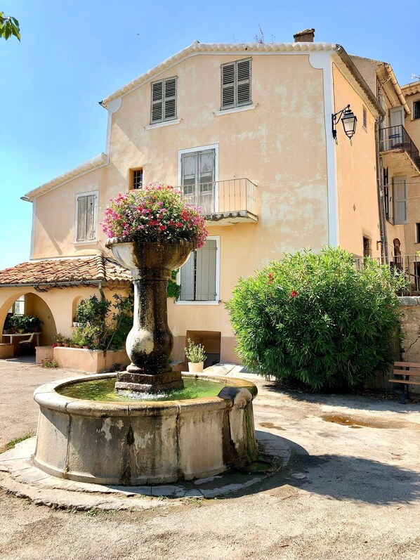 A building with a fountain, a balcony, and a window with shutters.