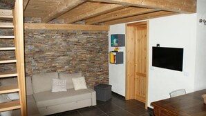 Ein gemütliches Wohnzimmer mit Backsteinwand, Holzboden, einer Couch mit Kissen, einem kleinen Tisch und einem an der Wand befestigten Fernseher.