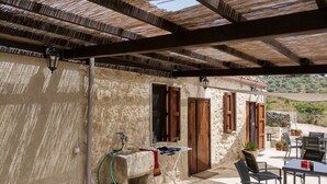 Ein überdachter Außenbereich mit Steinmauern, Holztüren und einem Tisch mit Stühlen.