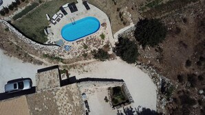 Eine Vogelperspektive auf ein Anwesen mit einem Schwimmbad, einer gepflasterten Terrasse und einer Steinmauer.