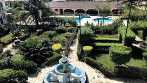 Un patio con una fuente central, rodeado de setos cuidados y palmeras.