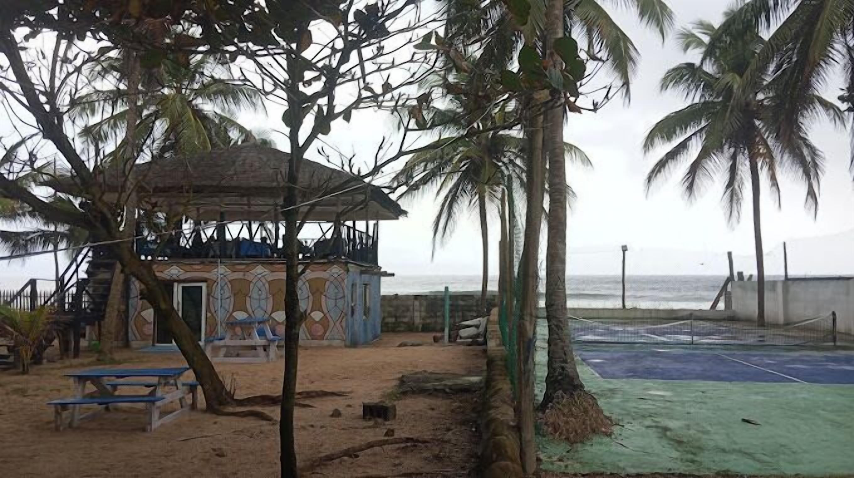 A beachside area with a small building, palm trees, and a tennis court.