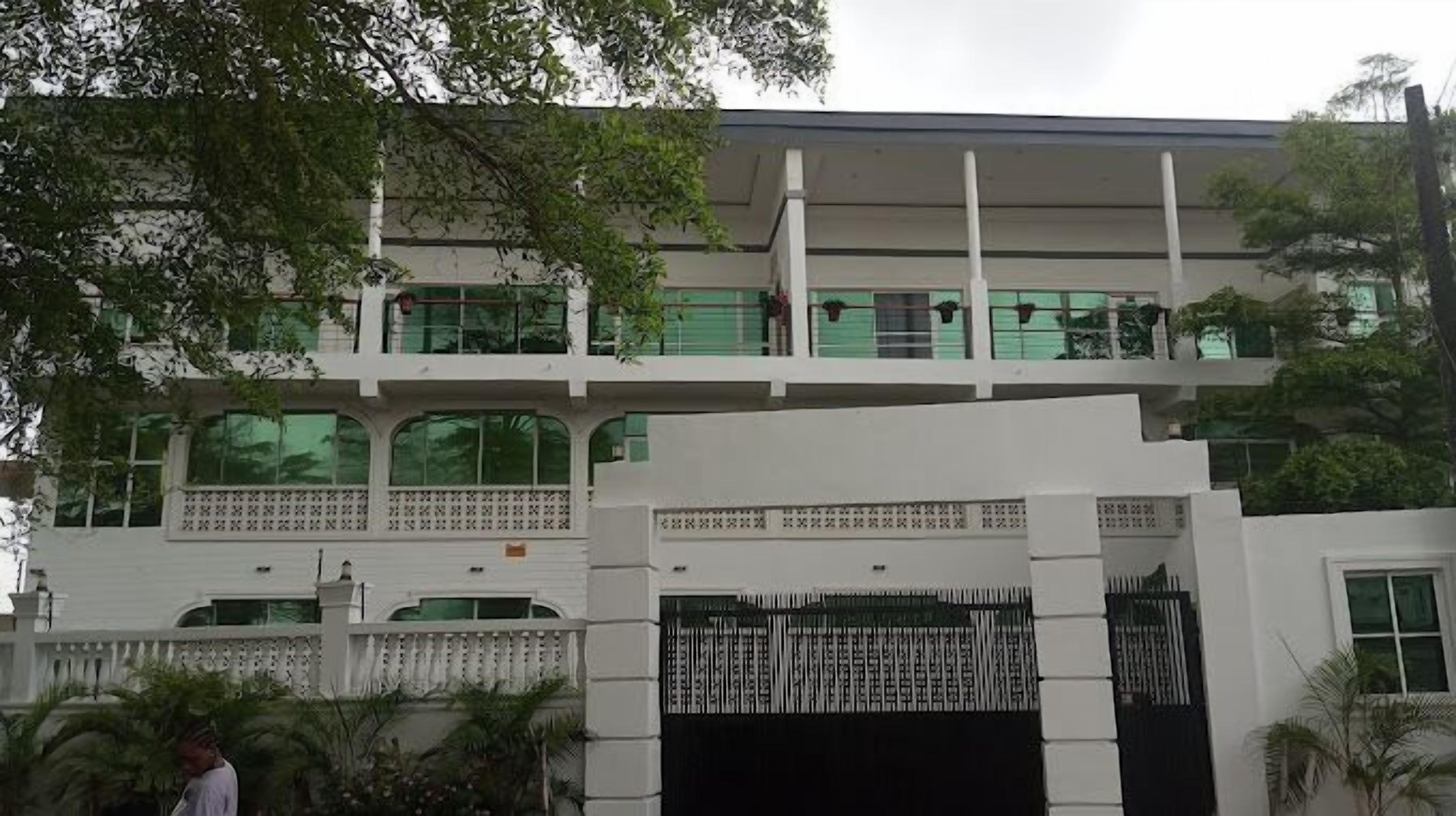 Un edificio de varios pisos con fachada blanca, ventanas amplias y entrada protegida por una reja.