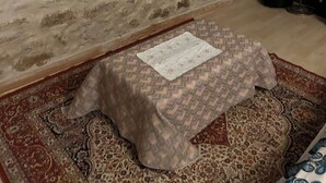 Una sala de estar con televisión, estante de madera, lámpara y alfombra estampada.