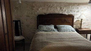 Un dormitorio con una cama de madera, una silla, una mesita de noche con lámpara y un armario.