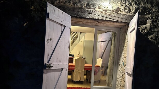 Una habitación rústica con puerta de madera, alfombra roja, cama y una mesa con sillas.