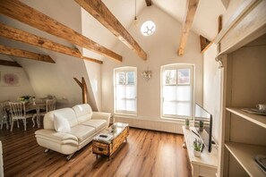 A spacious loft with exposed wooden beams, a white leather sofa, a wooden coffee table, and a dining area with a wooden table and chairs. - Central country house with loft character, WLAN & PP (Nordhorn)