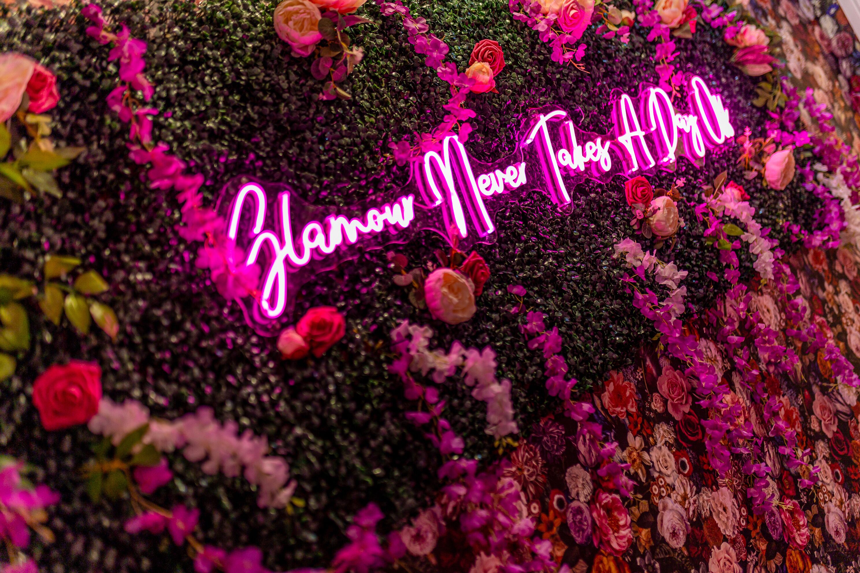 En neonlysende reklame med teksten 'Zamow Międre Pamięć' omgivet af forskellige blomster.