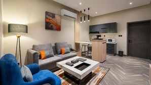 A modern living room with a sofa, coffee table, and a kitchen area with cabinets and a microwave. - Garden Millennium Hotel - Al-Salamah (Jeddah)