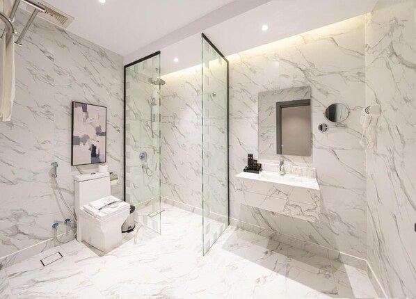 A modern bathroom with a glass-enclosed shower, a marble-tiled floor, a white toilet, and a vanity with a mirror and a hairdryer.