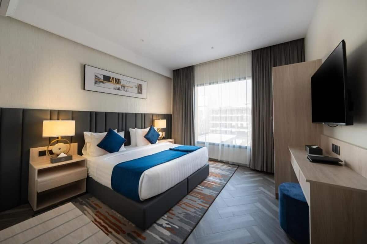 Habitación de hotel moderna con una cama grande, mesitas de noche, un televisor de pantalla plana y vistas a la ciudad.