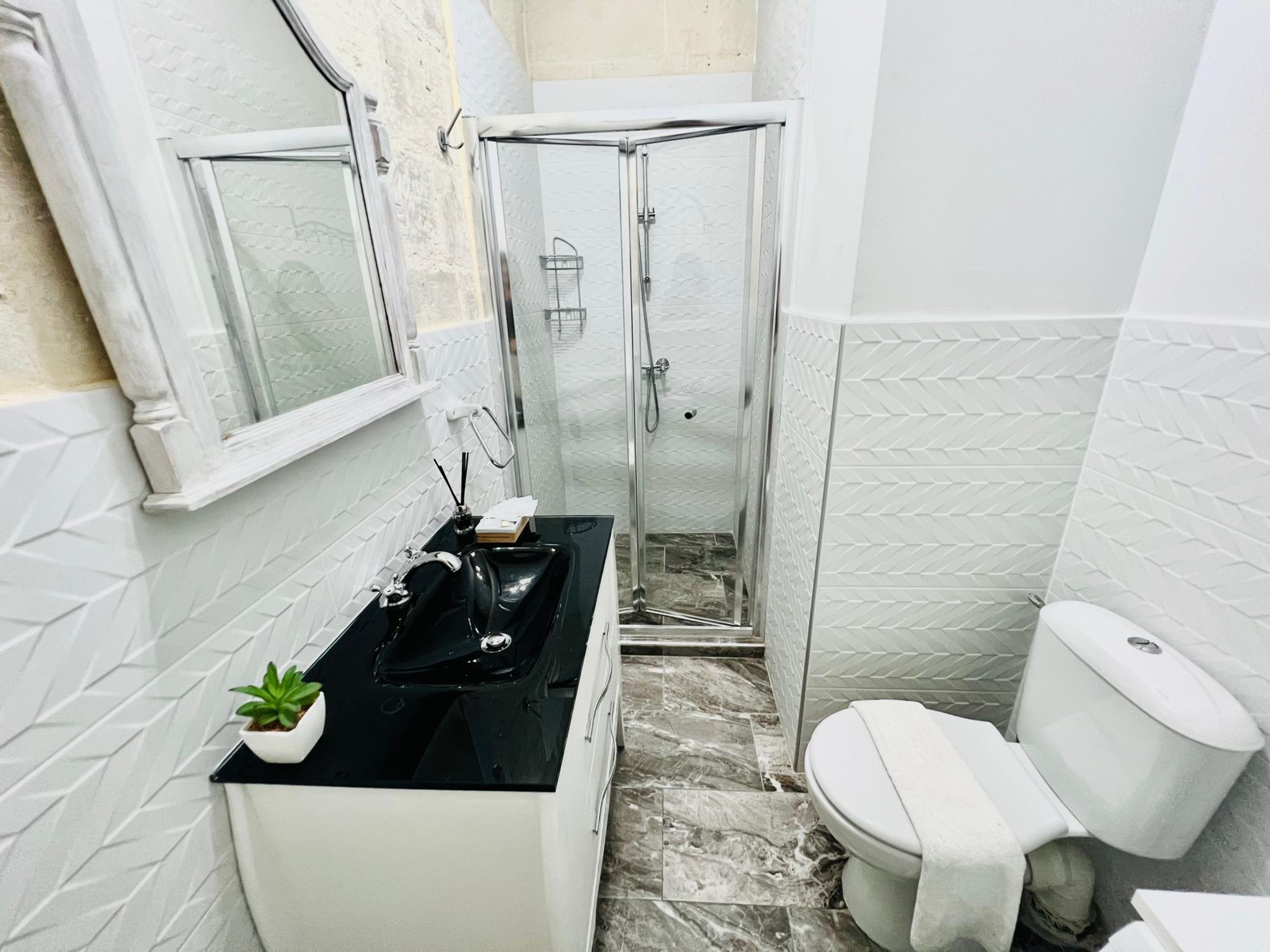 Une salle de bain avec une douche à parois de verre, un lavabo blanc doté d’un plan de toilette noir et des toilettes.
