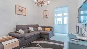 A modern living room with a grey sectional sofa, a small coffee table, a TV, and a chandelier. - Fairytale - Maltese Balcony - Separate Living Room (Valletta)