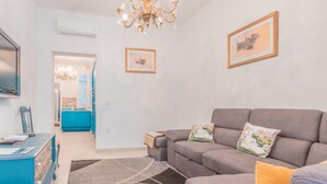 A living room with a grey sofa, a blue cabinet, a chandelier, and two framed pictures on the wall. - Fairytale - Maltese Balcony - Separate Living Room (Valletta)