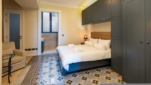 A bedroom with a bed, a nightstand, a lamp, a wardrobe, a chair, and a small table. - Luxury 2BR Valletta Apartment - Square Sea View (Valletta)