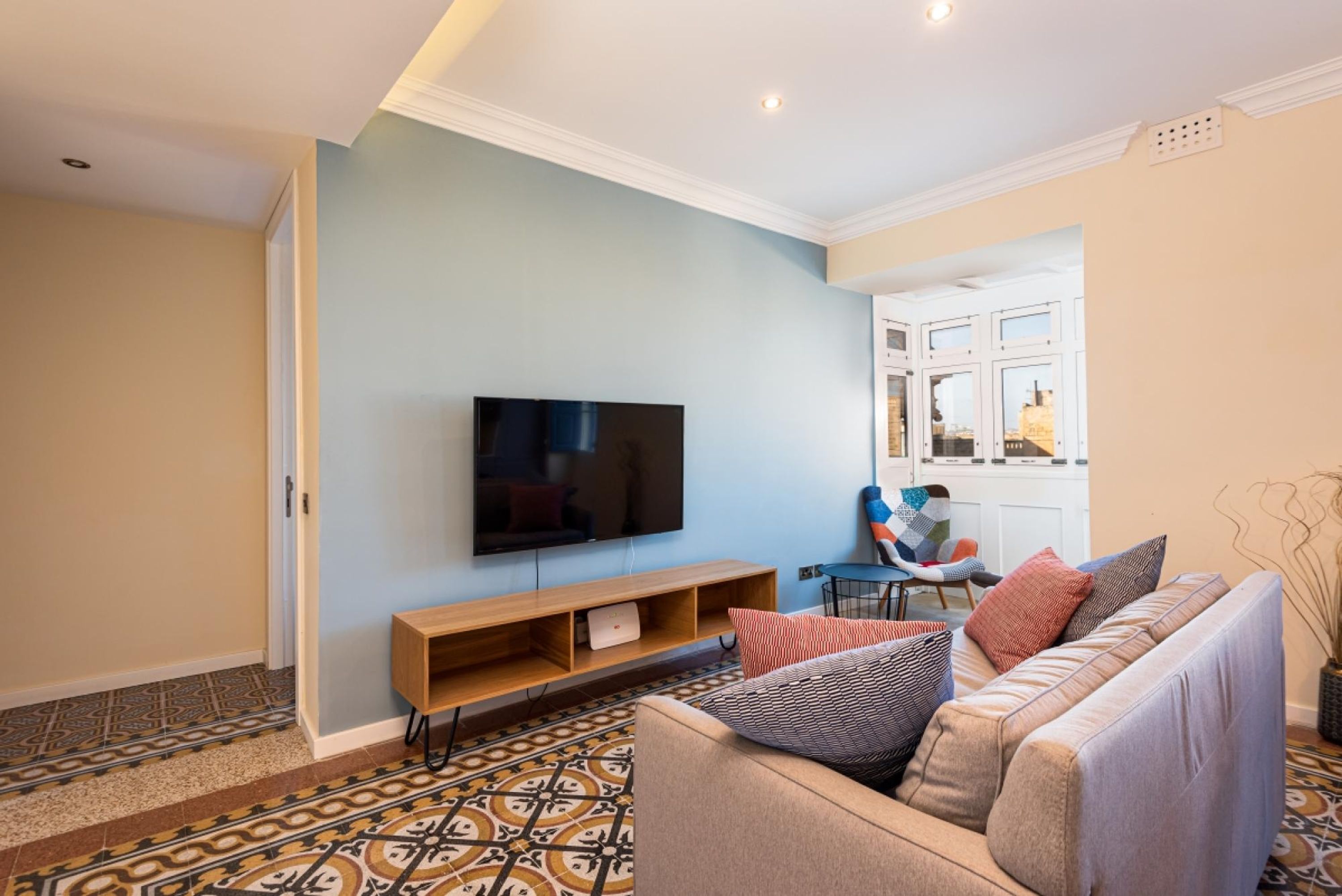 A living room with a flat-screen TV, a sofa, a patterned rug, and a window with a view.