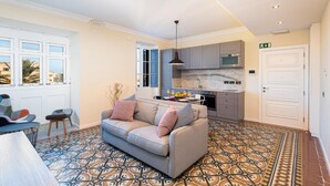 A spacious living area with a sofa, patterned floor, kitchen, and large windows. - Luxury 2BR Valletta Apartment - Square Sea View (Valletta)