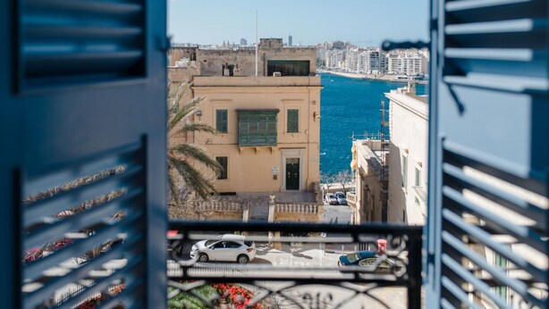 A view from a balcony overlooking a coastal cityscape with buildings and a body of water. - Luxury 2BR Valletta Apartment - Square Sea View (Valletta)