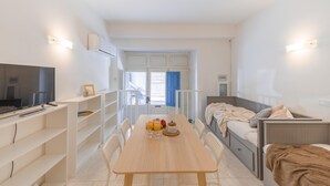 Habitación pequeña con mesa de madera, cama, televisor y balcón con puerta azul.