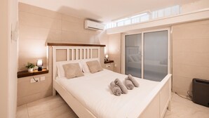 Un dormitorio moderno con una cama grande, mesitas de noche, un equipo de aire acondicionado, una ventana con persianas y vistas al exterior.
