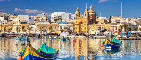 A waterfront cityscape with a prominent church and colorful boats in the foreground.