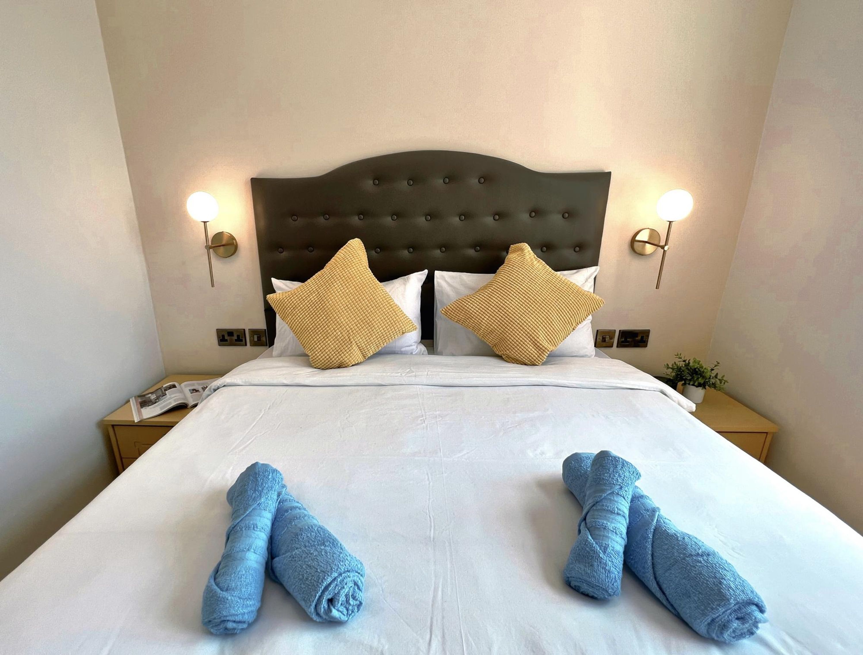 A hotel room with a large bed, two pillows, two nightstands, and a pair of towels.