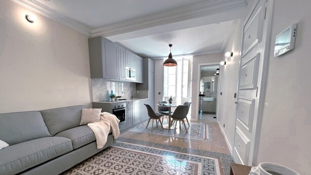 Une cuisine moderne avec des meubles gris, un coin repas comprenant une table et des chaises, et un canapé gris agrémenté d’un tapis à motifs.