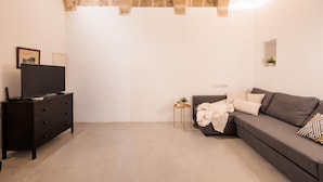 A modern living room with a grey sofa, a black TV stand, and a small side table with a plant. - Charming 1BR Apartment - Center Of Valletta (Valletta)