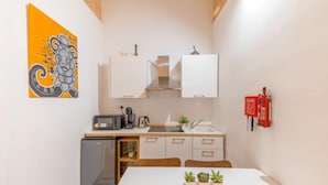 A compact kitchen with a refrigerator, stove, and sink. There is a small dining table with chairs and a few potted plants. A fire extinguisher is mounted on the wall. - Charming 1BR Apartment - Center Of Valletta (Valletta)