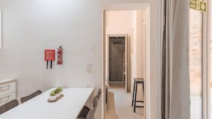 A modern room with a white table, chairs, a small plant, a fire extinguisher, and an exit sign. - Charming 1BR Apartment - Center Of Valletta (Valletta)