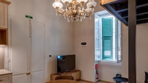 A dining area with a wooden table and chairs, a chandelier, and a television in the background. - Modern Luxury Studio Apartment (Sliema)