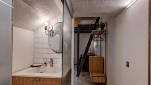 A modern bathroom with a wooden vanity, a round mirror, and a tiled backsplash. - Modern Luxury Studio Apartment (Sliema)
