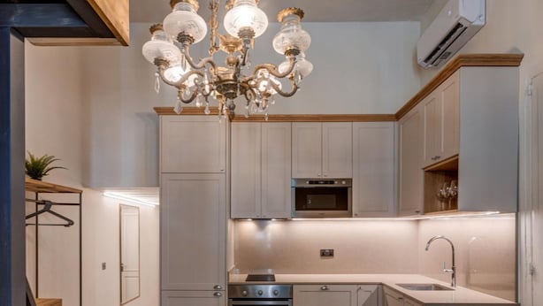 A modern kitchen with a chandelier, built-in appliances, and a dining area with a wooden table and chairs. - Modern Luxury Studio Apartment (Sliema)