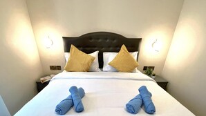 Una cama bien hecha con dos toallas dobladas en el centro, un cabecero oscuro y dos lámparas de noche.
