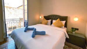 Una camera d'albergo con un letto, un comodino, una lampada a parete e vista su un balcone con ringhiera.