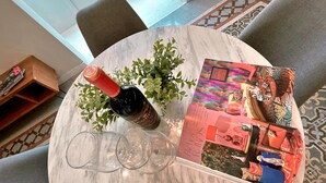 Une table ronde en marbre, avec une bouteille de vin, trois verres à vin et un magazine.