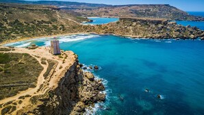Ένα παράκτιο τοπίο με έναν βραχώδη γκρεμό, έναν μικρό πύργο και μια παραλία.