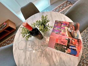 A round marble table with a bottle of wine, three wine glasses, and a magazine. - Local Gem Spacious 2BR 2BA Duplex Apartment (Valletta)