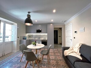 A modern kitchen with grey cabinets, a built-in oven, and a microwave. There is a dining area with a round table and four chairs. - Local Gem Spacious 2BR 2BA Duplex Apartment (Valletta)