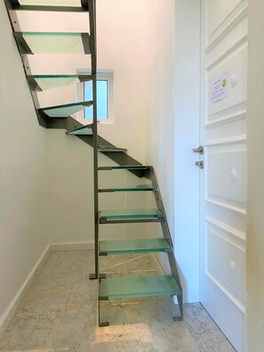A spiral staircase with glass steps and metal railings, leading to a door with a sign.