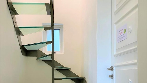 A spiral staircase with glass steps and metal railings, leading to a door with a sign. - Sea View Penthouse - Duplex (Valletta)