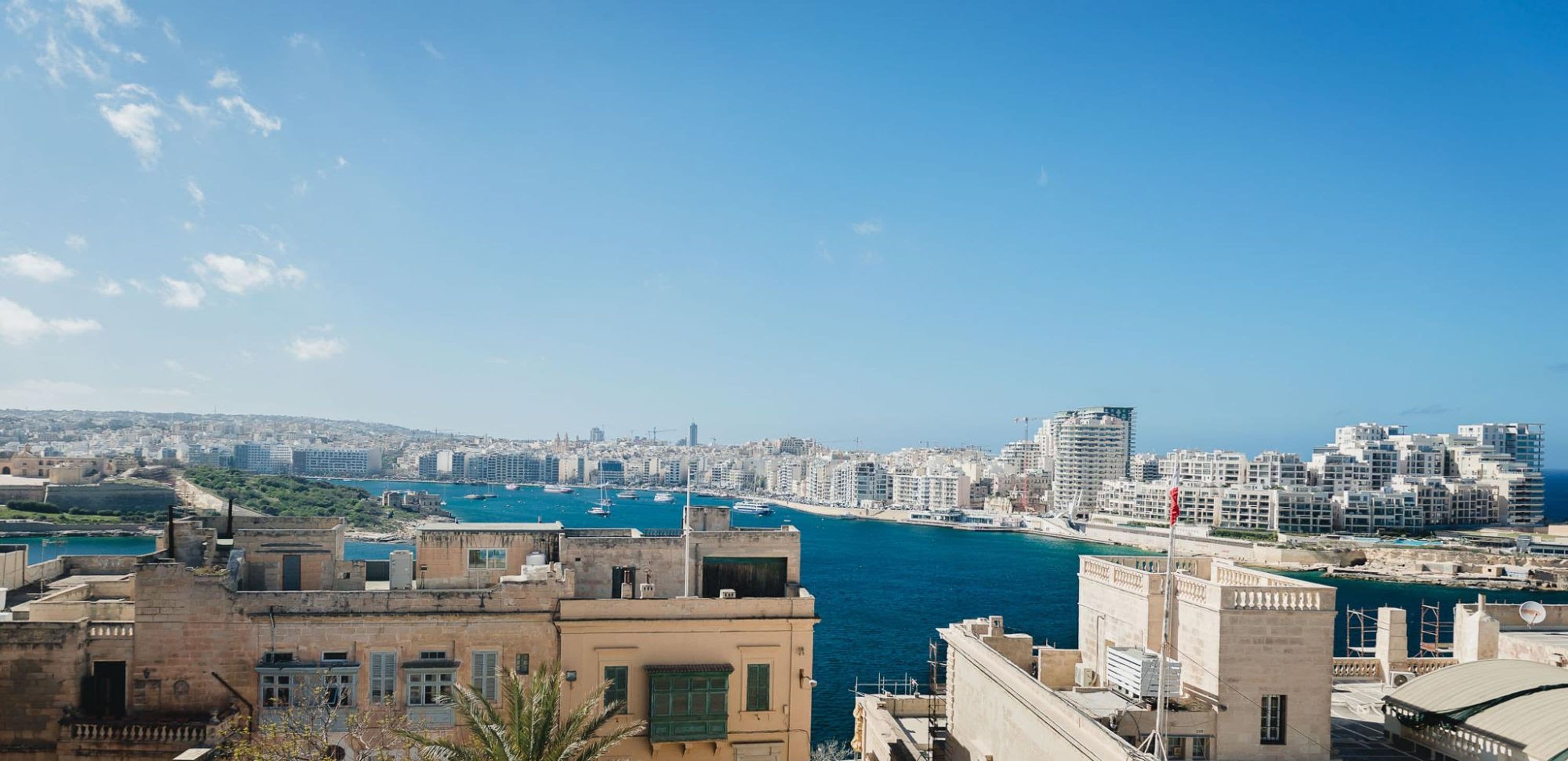 A coastal cityscape with buildings, a harbor, and a clear blue sky.