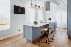 A modern kitchen with a large island, bar stools, pendant lights, and a flat-screen TV.