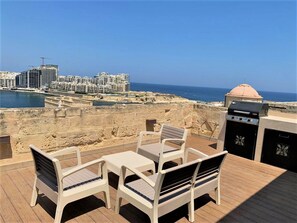 Eine Terrasse mit Sitzgelegenheiten im Freien und einem Grill, mit Blick auf die Stadt und das Meer.