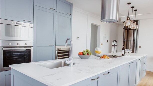 Een moderne keuken met een groot eiland, roestvrijstalen apparatuur en lichtblauwe kastjes.